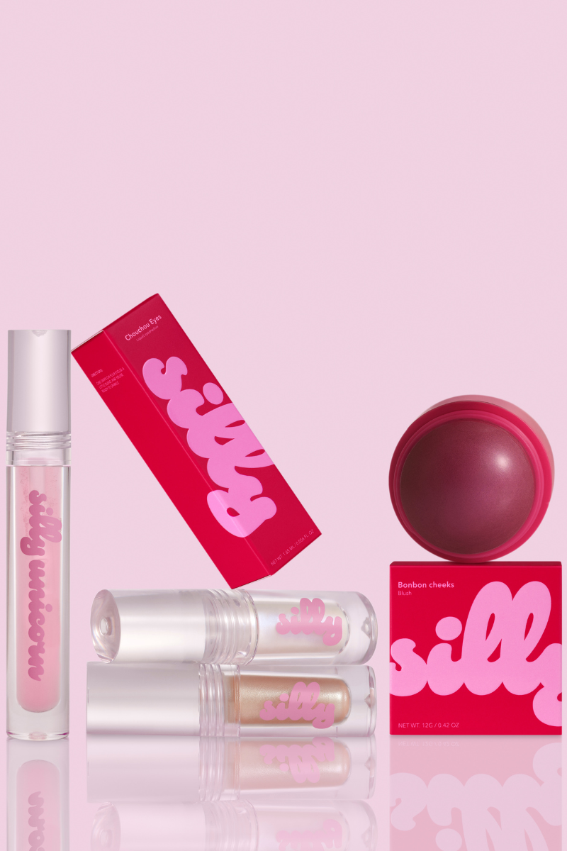 A beauty product set from the brand 'silly' on a light pink background, featuring a lip gloss tube, a boxed lip gloss stick, a lip gloss stick in a clear tube, a pink lip balm ball, and a pink box.